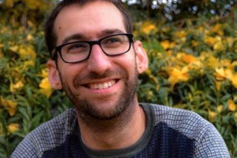 portrait profile pic of Noah Riseman black rimmed glasses beard grey and black top