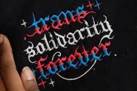 trans solidarity forever pink white blue writing black background next to thumb and forefinger