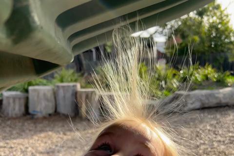 A child's hair standing up attracted to a plastic slide due to static electricity