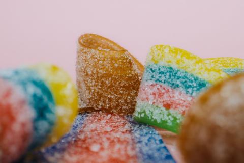 Vibrant close-up of multicoloured gummy candies with sugar coating on a pink backdrop.