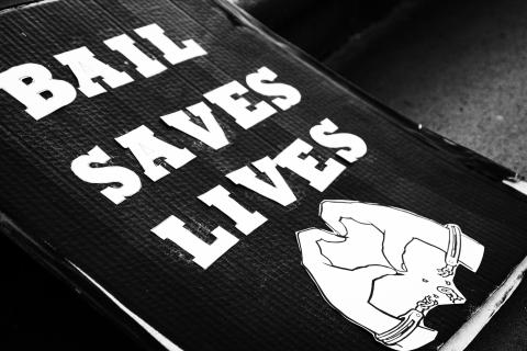 A black and white image of a poster with the words 'Bail Saves Lives' in capital letters. Beneath the text, there is an image of hands in cuffs forming the shape of a heart.