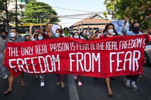 Protesters in Myanmar march behind a large red banner with white text reading "The only real prison is fear & the real freedom is freedom from fear"