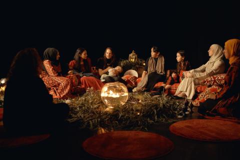 A photo of eight First Nations and Palestinian women and girls sitting in a circle. In the middle are leaves and candles.