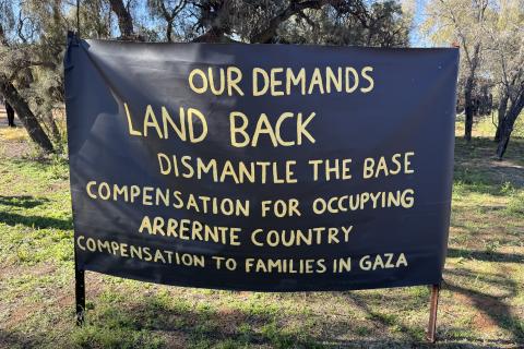 A photo depicting a banner with a list of demands from traditional owners on Arrente Country. There demands are listed as Land Back, dismantly the base, compensation for occupyin Arrernte Country and compansation to families in Gaza.