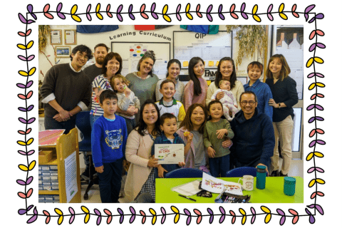 A group of Vietnamese adults and children in a classroom smiling at the camera.