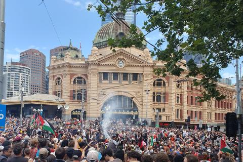 Smoke rises from near dancers at the centre of the crowd in front of Flinders Street station on Invasion Day 2024