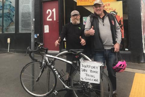 Val Nagle and Herschel Landes outside 3CR Community Radio with a sign supporting the safe cycling corridor in Glen Eira on Herschel's bicycle. 