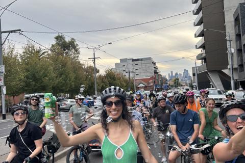 Group of bicycle riders riding on Bridge Road, Richmond, three people smiling at camera, centre person wearing green dress holding a bubble maker and surrounded by bubbles