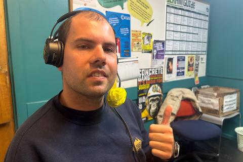 A young man wearing a headset does a thumbs up to the camera in the studio at 3CR
