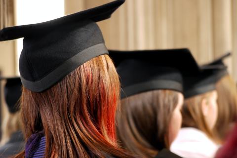 University students with long brown hair standing in a line with graduation caps on their heads