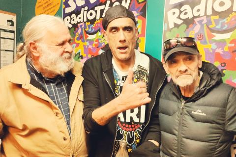 Robbie Thorpe stands next to fellow 3CR broadcaster, Gavin Moore, and host of Radical Australia, Joe Toscano. Robbie and and Gavin look straight ahead. Gavin gives a thumbs-up gesture. Joe looks sideways at Robbie and Gavin