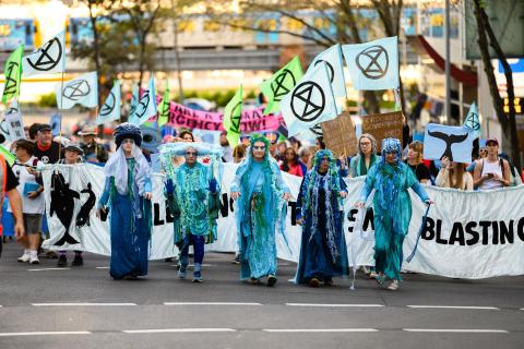 A photograph of five people in bright blue costumes in front of protesters fighting against seismic blasting off Victoria's coast. // Image credit: Julian Meehan