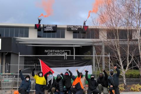 Photo of protester outside Northrop Grumman manufacturers in Canberra. Two Banners hanging from the front of the building read "GRUMMAN ARMS ISRAEL, SANCTION NOW".