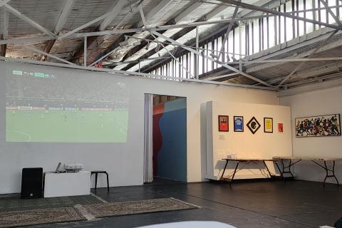 Image of world cup football game projected on wall of Lil Homey Cafe with artwork adjacent wall