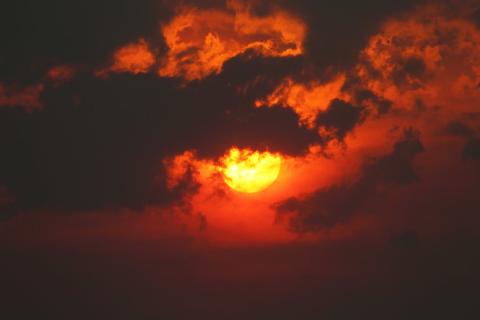 A dark orange sun shines through smoke clouds, turning the sky red. 