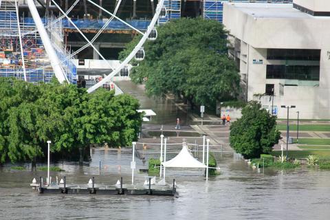 Photo of Brisbane's Southbank during the 2011 floods. Floods engulfing green trees, white ferris wheel, blue construction and grey buildings.