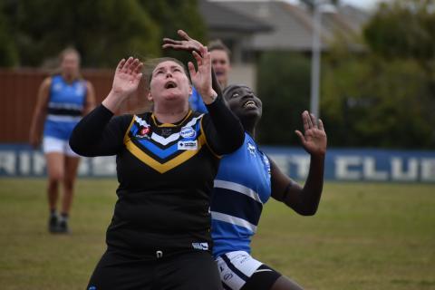 Rucks from Caroline Springs and Point Cook Centrals in a stoppage contest, during the last round of the home and away season of the WRFL VU Polytechnic Senior Women’s Competition. The photograph depicts two women footy players from opposing teams, one Black and one white, looking intently upwards and reaching towards a football that is out of frame.
