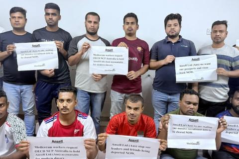 Bangladeshi migrant workers hold signs demanding Ansell take responsibility for addressing MediCeram labour violations.