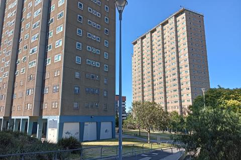 Public housing towers - one in partial view in the foreground, and one in full view in the background. It is a sunny day with a clear blue sky.