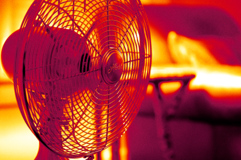 Electric fan in front of a bed, against red and orange background showing heat