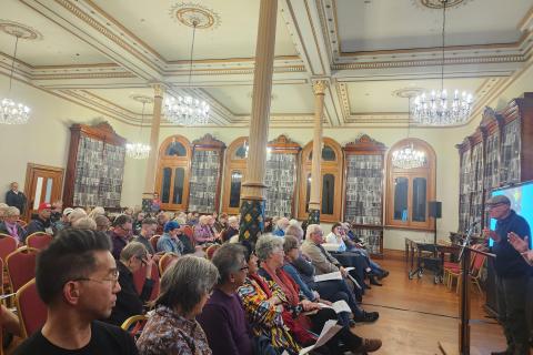 Town Hall meeting members sitting down looking at speaker at the front.