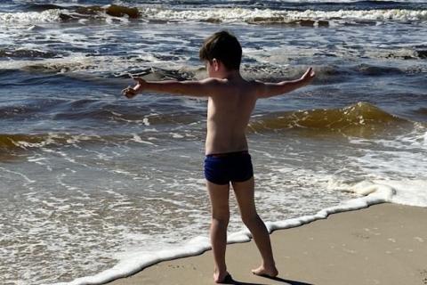 Young child standing with arms wide open towards the ocean