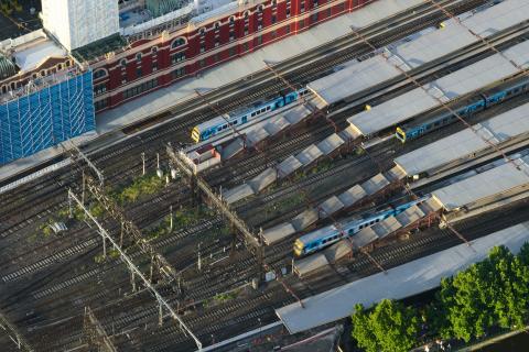 Aerial photo of approximately twelve platform roofs and railway tracks, Flinders Street Railway station in Melbourne, Australia. There are some metropolitan passenger trains both stationary and moving through some of the platforms.
