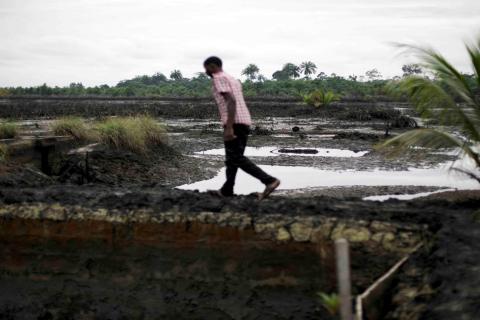 A man walks across a field polluted by oil