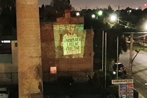 a projection on a  wall that said phones are a life line free the refugees 