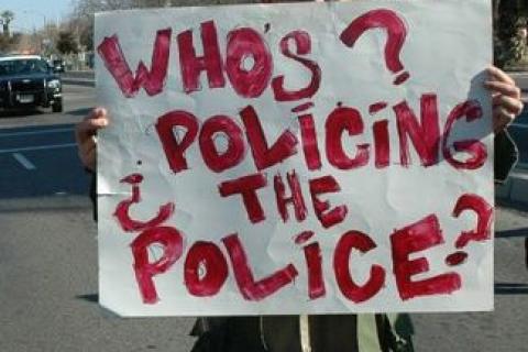 a person holding up a sign stating whos policing the police 