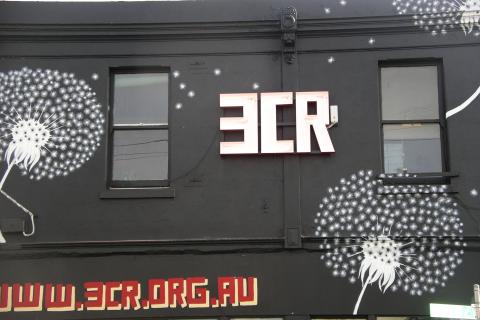 A photograph of the from of the 3CR building in Fitzroy, with large drawings of dandelions, a large neon sign that says 3CR and smaller text painted below which reads www.3cr.org.au