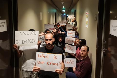 picture of Medevac refugees. inside  the hotel holding protest signs one said what is our crime
