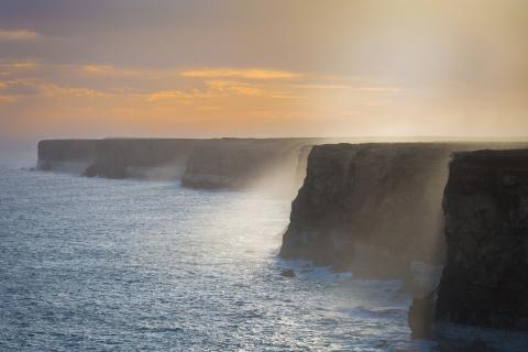 Sea washing up against steep cliffs at sunset