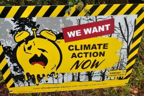 A yellow and black sign with a melting clock with alarmed face. Climate Action Now