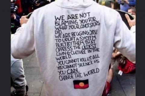 Photograph of protestor's torso from the back. They are wearing a hoodie that says "We are not blaming you for what your ancestors did. We are begging you to uplift a system built by them that oppress the oldest living culture in the world. You can not kill us all. You can not silence us. You can change the world.