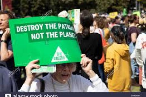 An elderly white woman at a protest holds a sign reading "Destroy the patriarchy, not the planet"