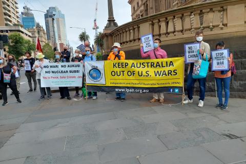 About 20 people standing with banners in front of the Old Treasury building, a white banner on left reads - No War, No AUKUS, No nuclear subs, yes to peace, safer climate jobs, in the centre is a yellow banner with the IPAN logo and the words - Keep Australia out of US wars, Independent and Peaceful Australia Network.