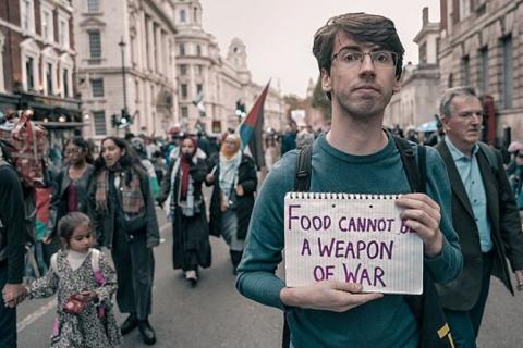 A man holding a sign which is written on it "Food cannot be a weapon of war"