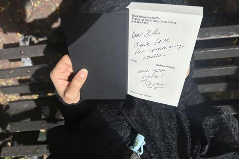 Aerial close up view of someone opening the cover page of Black Thoughts Matter, hand-signed by Chelsea Watego the handwriting  reads Dear 3CR, thank fuck for Community Radio - Love your work! Chelsea