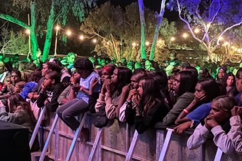 A crowd of people gathered at the foot of a rock concert stage in the outdoors at night