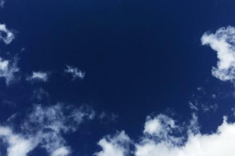 Looking up into an empty blue sky, fringed with white clouds