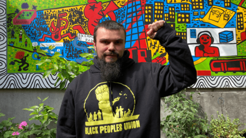 Keiran Stewart-Assheton in the 3CR garden wearing a Black Peoples Union hoodie and holding up a raised fist