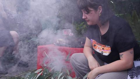 Brittney Henderson squatting next to the sacred flame at a Smoking Ceremony, gazing pensivley into the flame.