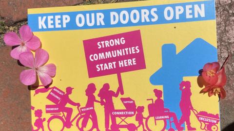 I mage of the post card mentioned in the interview. It features the words 'Keep Our Doors Open, Strong Communities Start Here." Includes image of a diverse looking community entering a neighbourhood house.