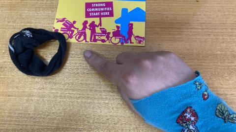Image of the Neighbourhood Housing Postcard with a hair tie and glove made from socks
