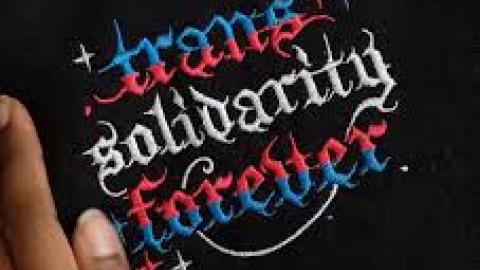 trans solidarity forever pink white blue writing black background next to thumb and forefinger