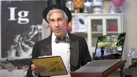 Ig Nobel prize emcee Marc Abraham at the lecturn with a top hat and clipboard