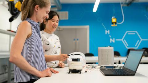 Two women working with tech on a white desk