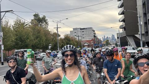 Group of bicycle riders riding on Bridge Road, Richmond, three people smiling at camera, centre person wearing green dress holding a bubble maker and surrounded by bubbles