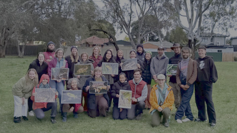 A photo of a group of DCMC's volunteers, smiling and showing images of frogs found at Darebin Creek. Provided by Darebin Creek Management Committee.